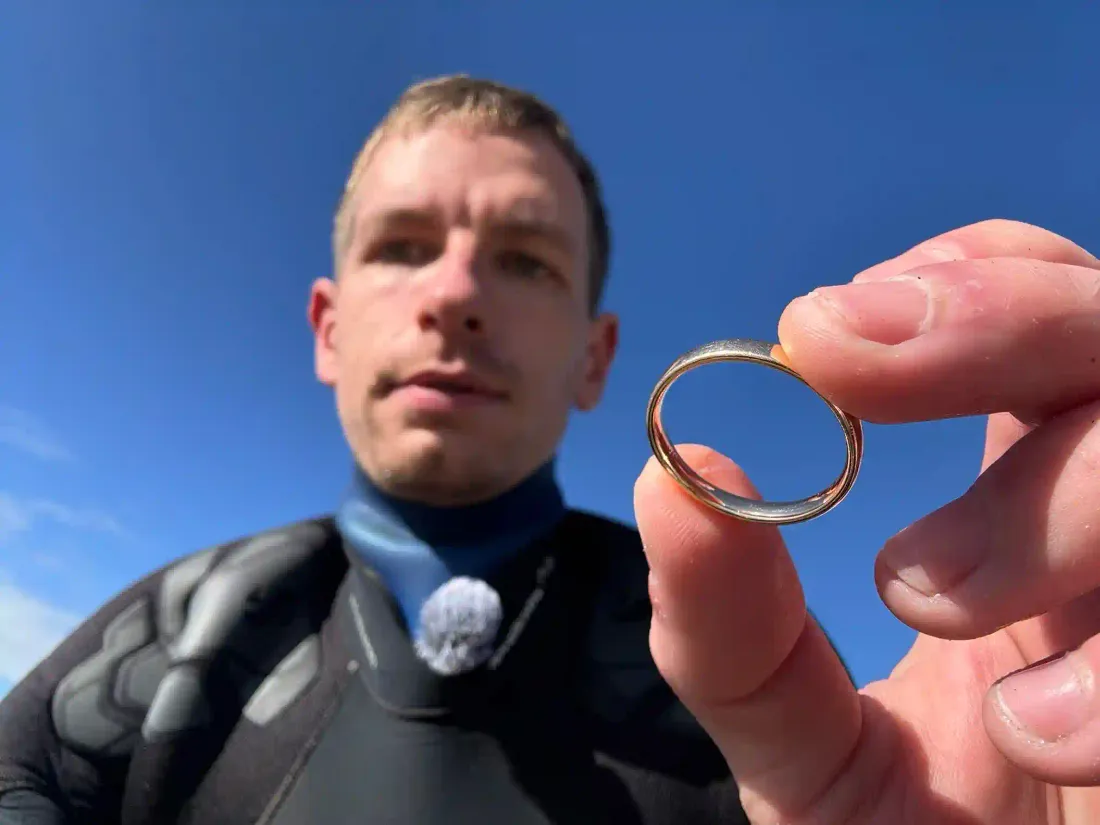 Taucher hält einen aus dem Wasser geborgenen Goldring vor blauen Himmel