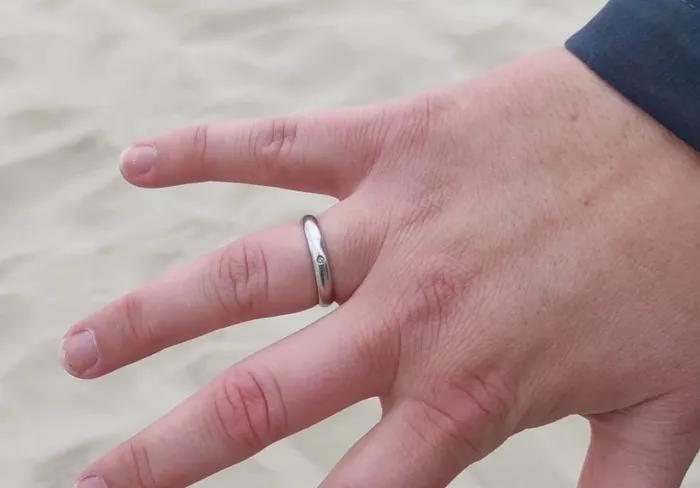 Hand mit wiedergefundenem Ehering vor hellem Strandsand
