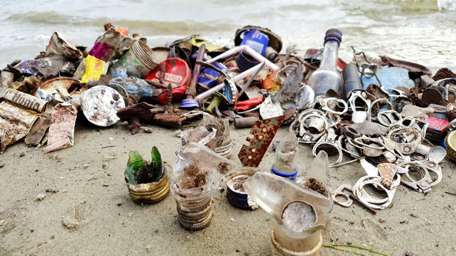 Tagesausbeute einer Strandsuche im Sand: Schmuck, Münzen und eingesammelter Unrat