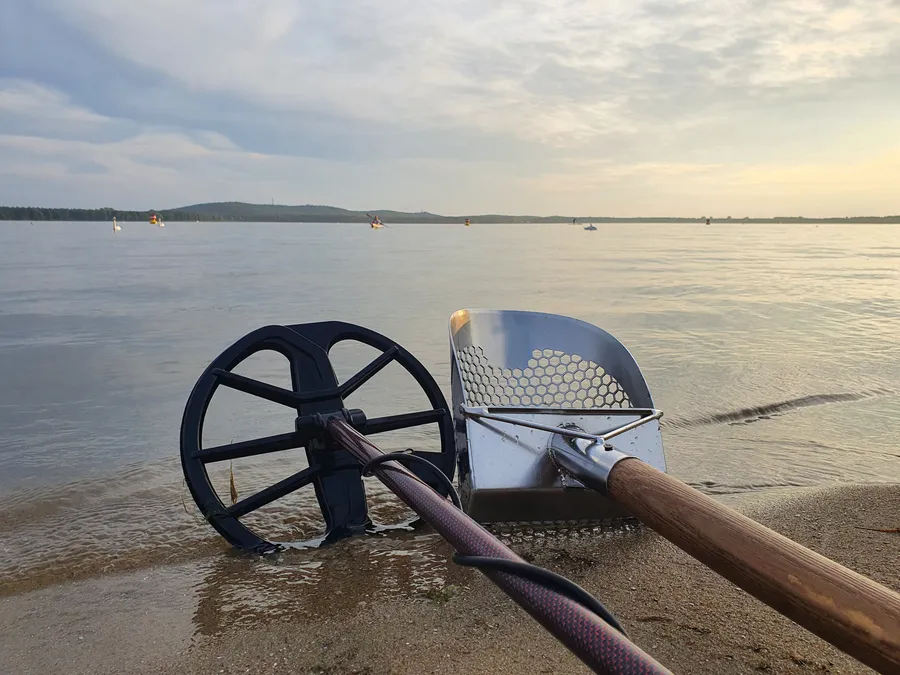 Detektorspule und Sandschaufel am Wassersaum im Abendlicht